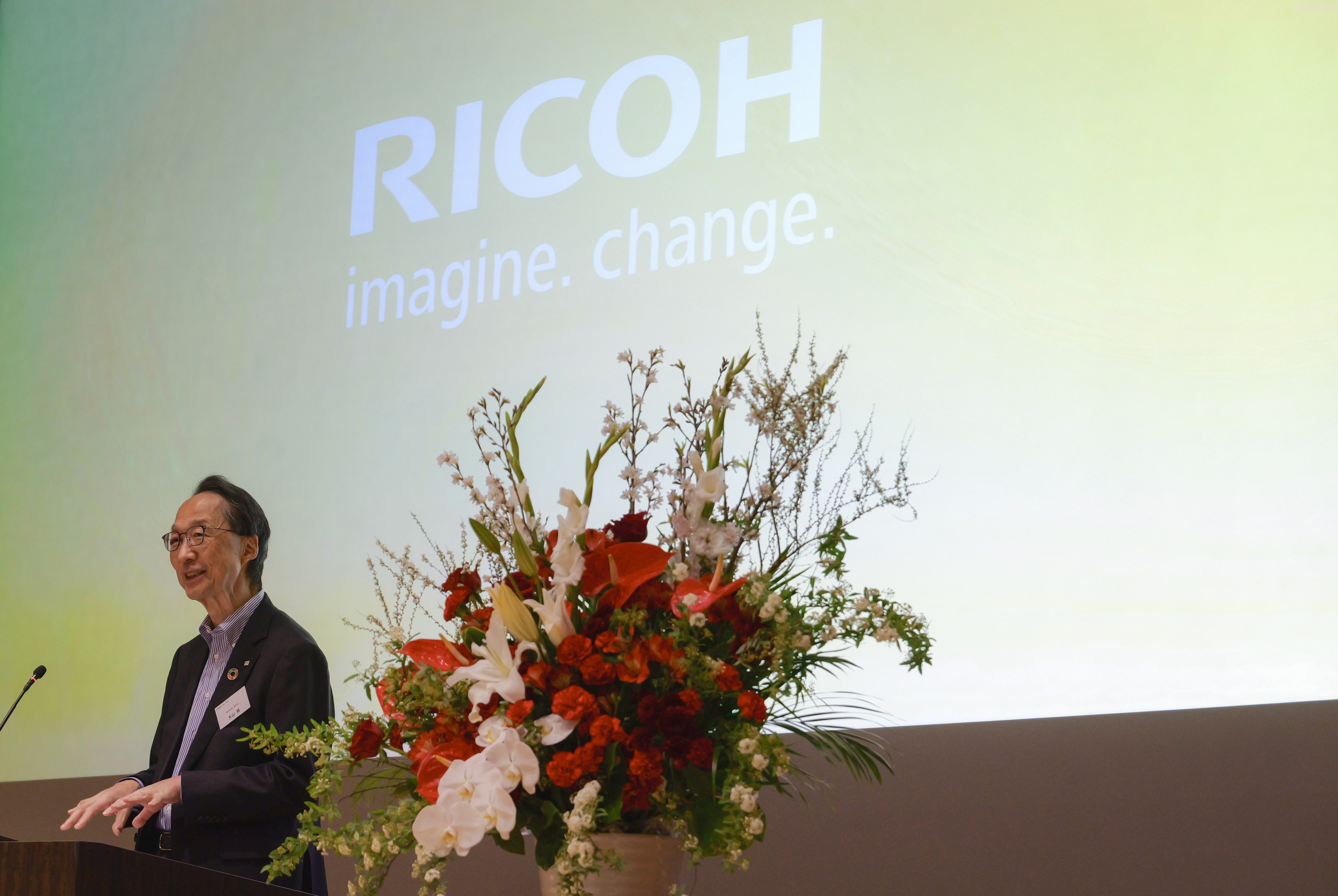 サイネージを背景に挨拶をする大山社長